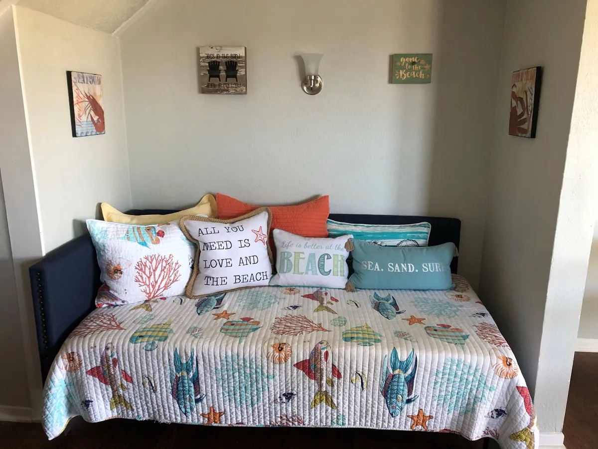 A cheerful living area with decorative pillows, a bed quilt, and wall art. The space is arranged to encourage socializing and relaxing, creating a welcoming atmosphere for group gatherings after a day of beach activities.