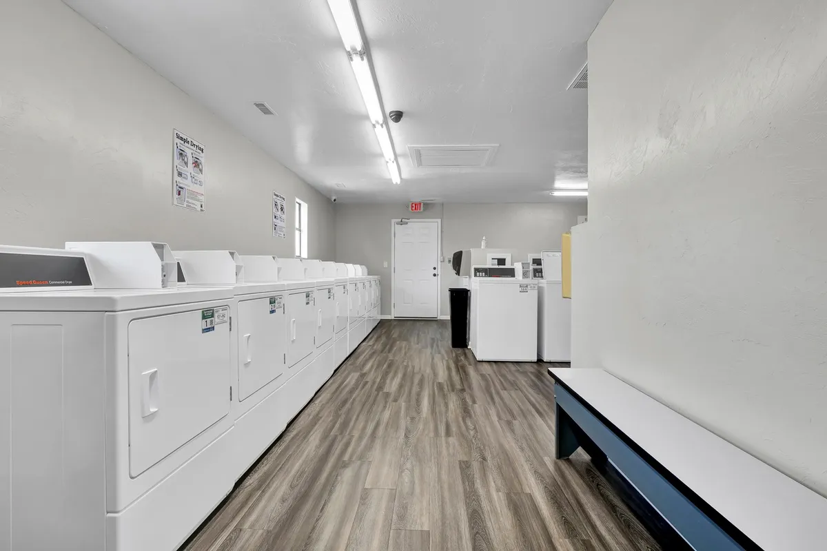 An organized interior laundry room with a row of washing machines, dryers, and a seating bench for guests to use while waiting for laundry. The room is well-lit and efficient, emphasizing convenience and comfort for extended stays.