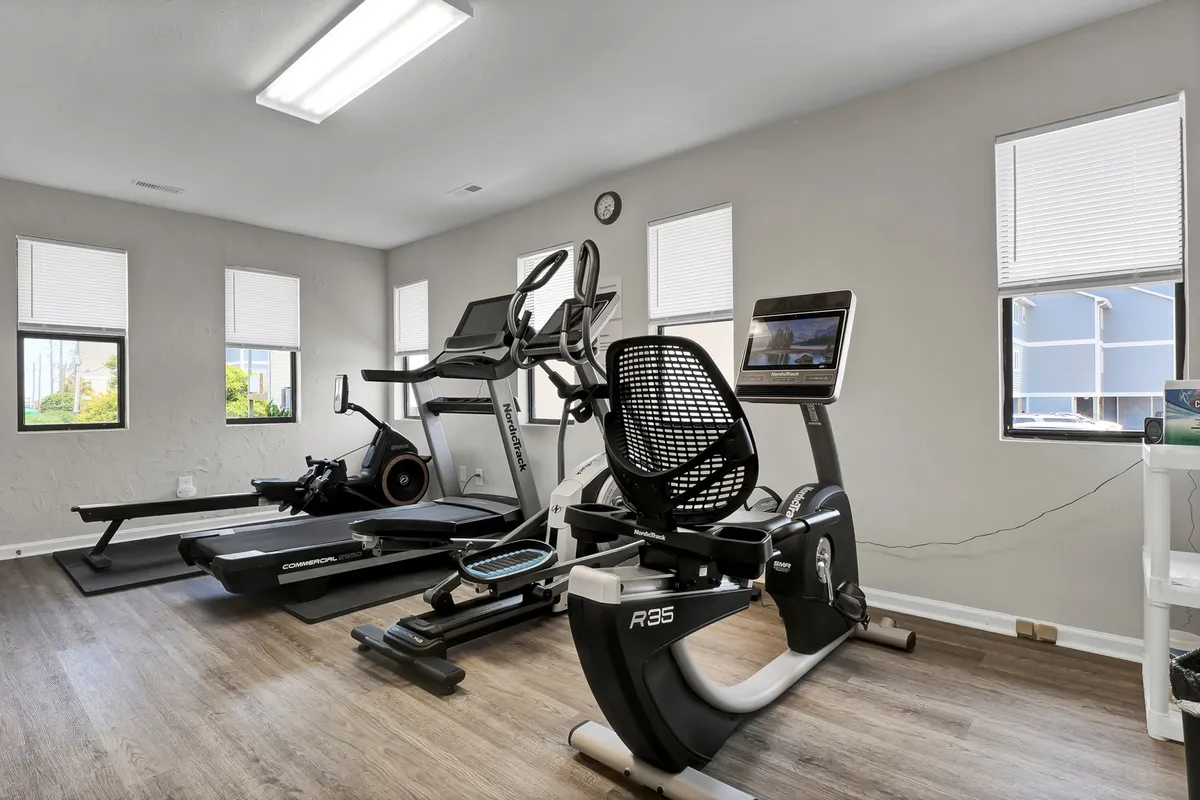 A bright fitness room with exercise equipment, large windows, and a clock, offering an opportunity for guests to work out or stretch together before or after outdoor adventures.