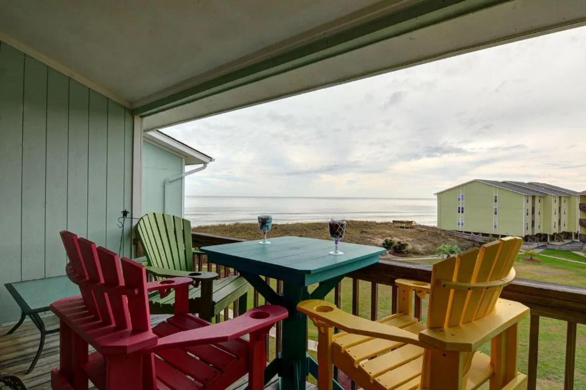 The image features a cheerful arrangement of colorful adirondack chairs and a table set with drinks, all overlooking a stunning ocean view. The inviting setup suggests a perfect spot for relaxing, socializing, and savoring either a sunrise coffee or a sunset toast with loved ones.