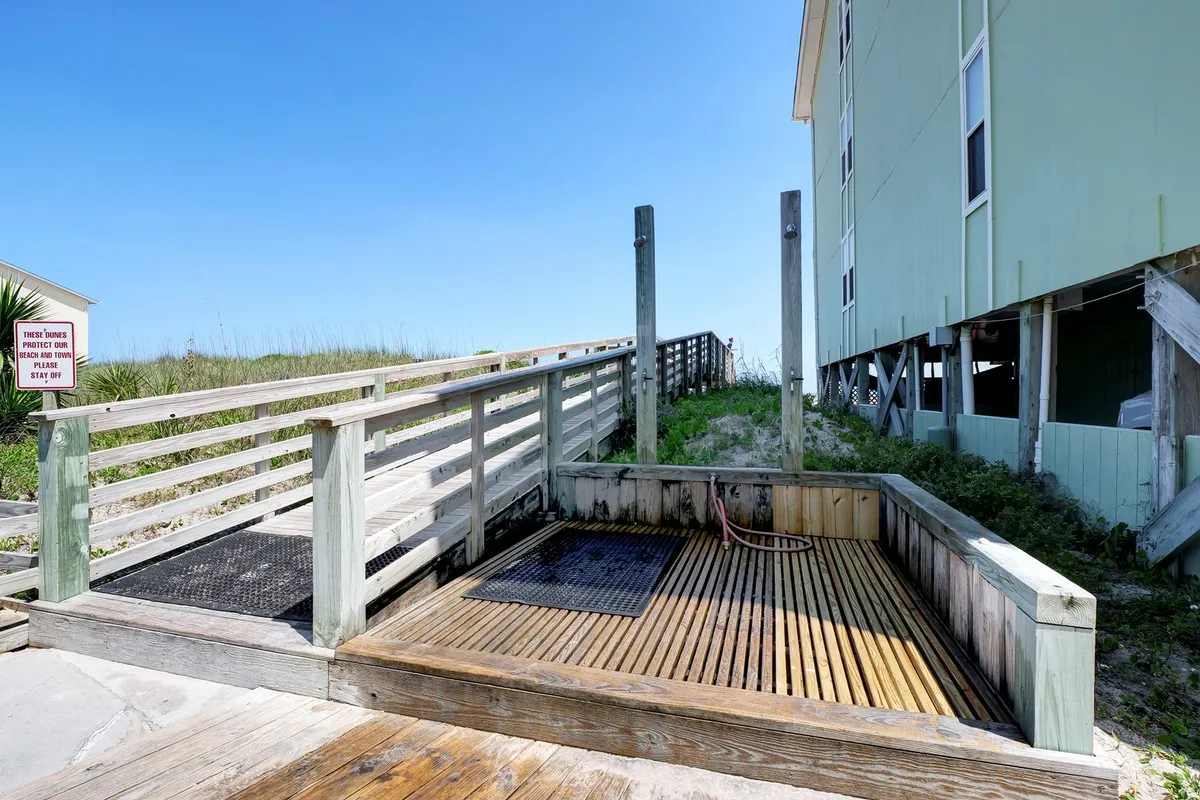 A wooden deck with a shower area and ramp leading directly to private beach access. The inviting outdoor setup encourages rinsing off after ocean adventures and seamless transition between the beach and condo amenities.