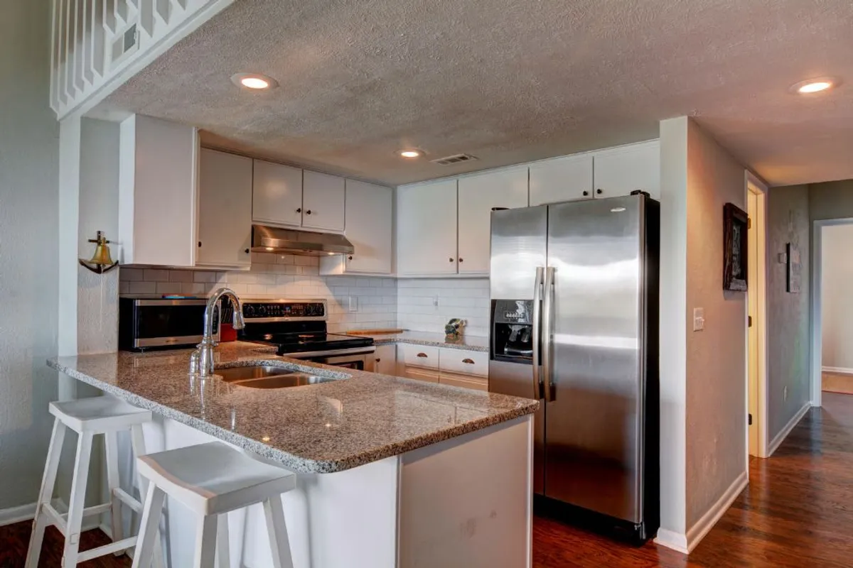A spacious, modern kitchen featuring a granite countertop, stainless steel appliances, and a central kitchen island. The warm lighting and open design invite guests to cook together and enjoy conversations around the island.