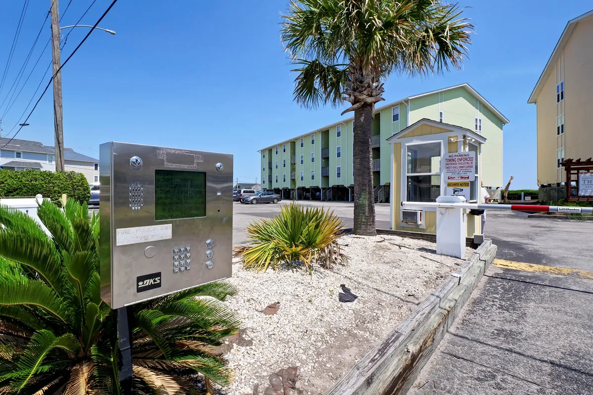 An exterior view of the property's entrance features an intercom system, palm trees, an entrance booth, and a well-maintained parking area. The friendly, accessible vibe signals an exclusive yet welcoming environment for couples seeking a peaceful retreat.
